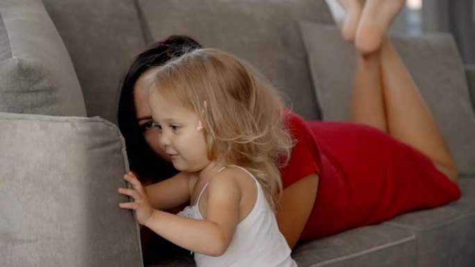 微笑的美女躺在沙发上，用智能手机展示可爱的小女孩