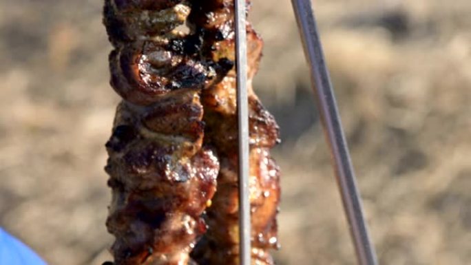 野餐时，用小刀将烤架上的新鲜猪肉烤肉从烤串中取出，放在开阔的天空下的盘子里。高加索户外食物和烧烤概念