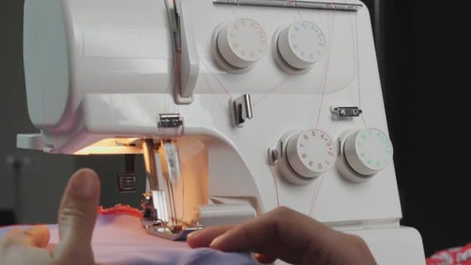 女设计师在缝纫机上工作。女人的手缝制时尚衣服，特写。创造和剪裁服装。overlock机器的详细信息