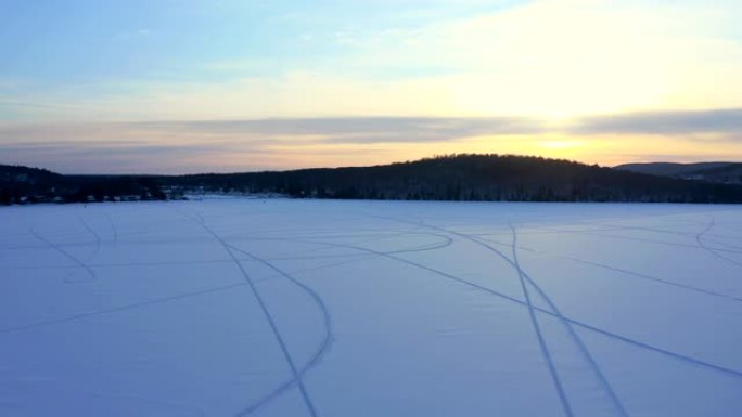 加拿大魁北克日落时雪上有雪地摩托痕迹的湖泊的4k航拍视频视图