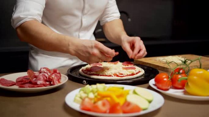 追踪无法识别的厨师将萨拉米或意大利辣香肠切片放在未完成的披萨上的特写镜头，站在餐厅厨房的桌子上，上面