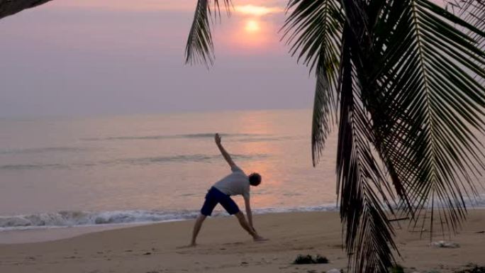 灵活的人在黄昏或黎明在海滩上练习三角瑜伽姿势