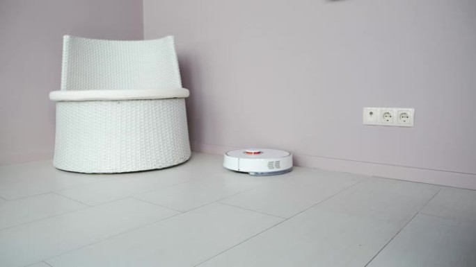 白色机器人真空吸尘器正在用吸尘器吸尘瓷砖地板。智能家居。机器人真空吸尘器在室内进行自动清洁