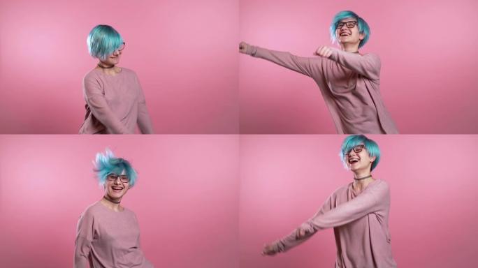 蓝色头发不寻常的女人在粉红色背景下在工作室里玩得开心，微笑，跳舞的模因时尚社交网络跳舞。音乐，舞蹈概