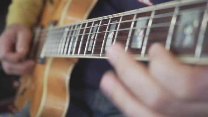 吉他大师的手在脖子上滑动的特写镜头，在天然轻质木材的半声学空心体吉他上弹奏和弦，音阶和独奏