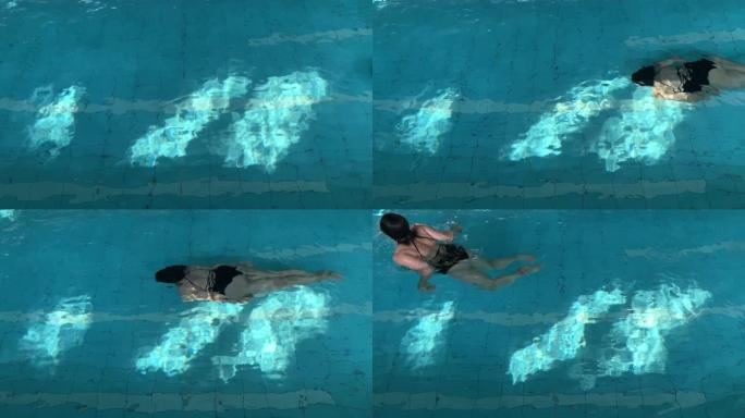 女人在阳光下的游泳池里水下游泳