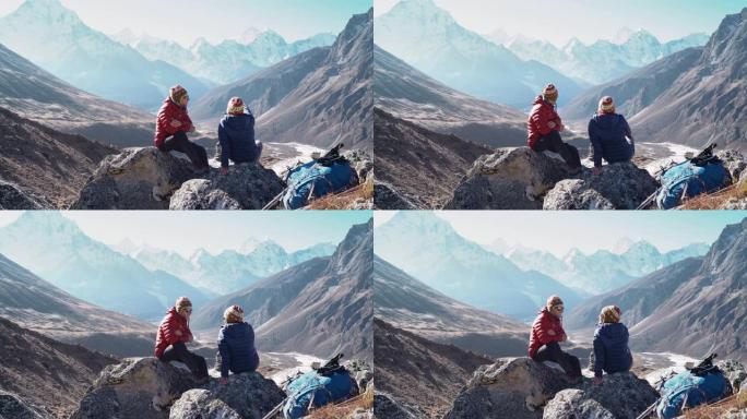 年轻夫妇坐在石头上，说话，休息在Dughla 4620米附近的珠穆朗玛峰大本营徒步旅行路线。他们留下