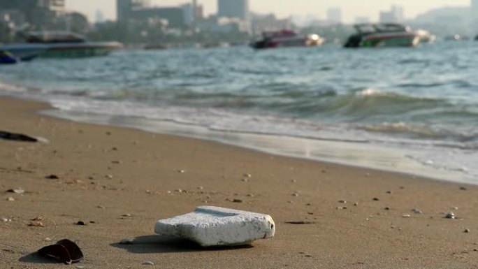 海滩上的泡沫塑料橡胶和废物留在海滩上，海浪将它们吹入海中