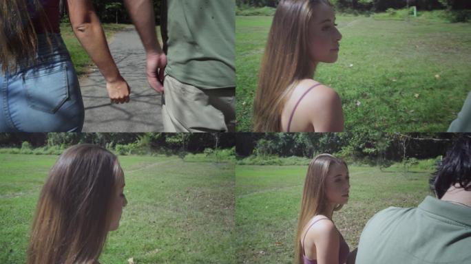 跟踪镜头。公园里的一对年轻夫妇牵着手，直到一个电话打断了他们。