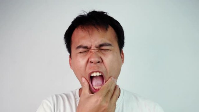 特写亚洲男子闭着眼睛的肖像，触摸他的脸颊，患有牙痛。他因蛀牙或牙龈肿胀而感到牙齿疼痛。情感和表达概念