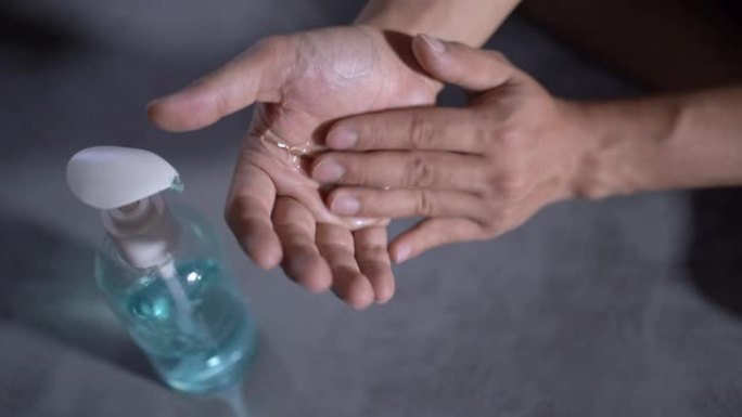 4k亚洲男性手在家中客厅使用洗手液凝胶，自我检疫，蓝色酒精凝胶，灰色背景，杀灭细菌，洗手，敲击泵瓶，