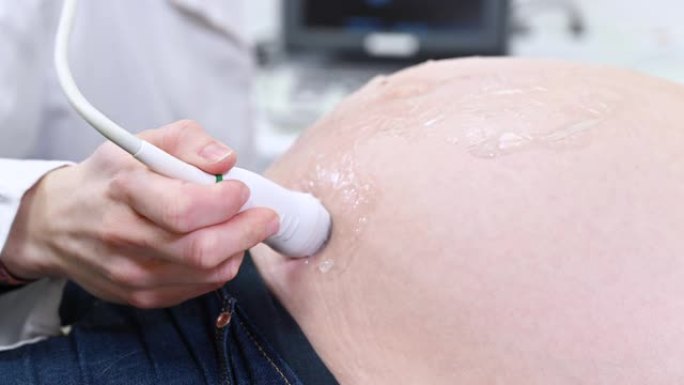 医生对医院的孕妇进行超声或超声检查，近距离拍摄产科医生在未来母亲的腹部移动换能器。