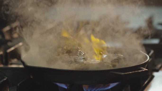 专业厨师烹饪flambe风格。在明火锅中准备盘子肉。厨师在商用厨房的煤气灶上油炸食物。男人在餐厅的滚