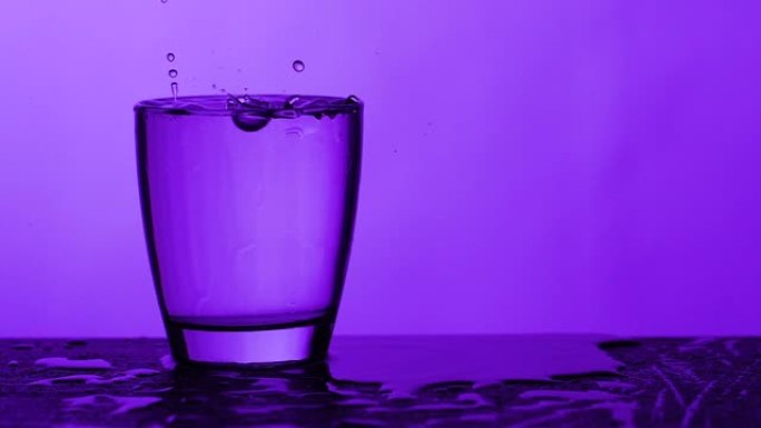 雨滴落在装满水的玻璃上-紫色背景，慢动作
