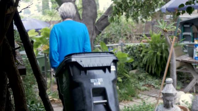 一位活跃的老年人将一个空的垃圾桶放到他的院子里