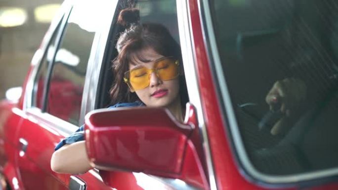 年轻的旅游女人在旧红色汽车上休息和睡觉，时髦的人和另类生活方式的概念