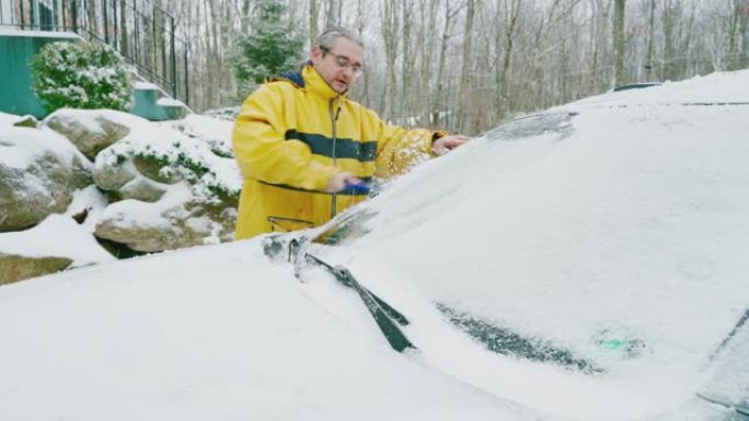 成熟的男人在冰雪中清洗汽车。