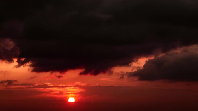 橙色的大太阳的时间流逝，落在红色天空的地平线上，灰色的乌云密布。4k镜头。