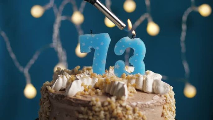 蓝色背景上有73号蜡烛的生日蛋糕。蜡烛着火了。慢动作和特写视图