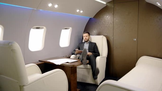 律师成功的人在私人飞机上坐下并在平板电脑上阅读新闻的肖像。企业家飞机