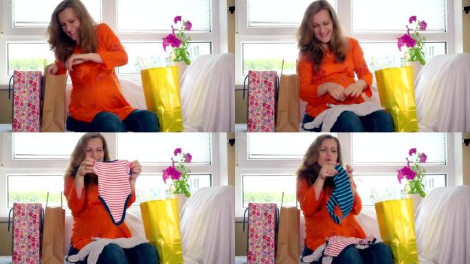 购物后快乐怀孕的女性坐在沙发上看婴儿衣服