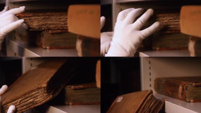 白色棉质手套的特写镜头从博物馆或私人图书馆的书架上取下非常旧的书。库存镜头。探索古老的泛黄书籍