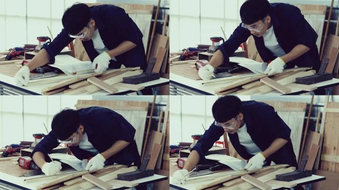 亚洲男子木匠在家里用木工工具和木头躺在车间里用技术图纸或蓝图施工纸工作