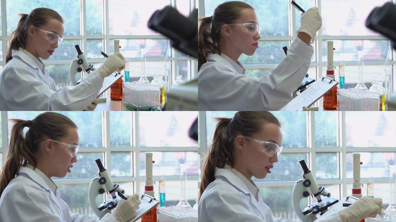 放大视频拍摄的年轻女科学家拿着试管进行分析，并用笔将结果记录在纸上。