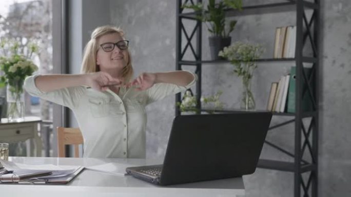 在线商务，快乐迷人的女孩自由职业者在办公室的一台笔记本电脑上工作，室内有美丽的鲜花，然后耸耸肩，为完