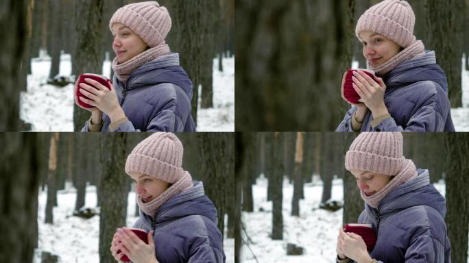 年轻美丽的女人的特写镜头在冬季松树林中用热茶杯温暖双手。4K