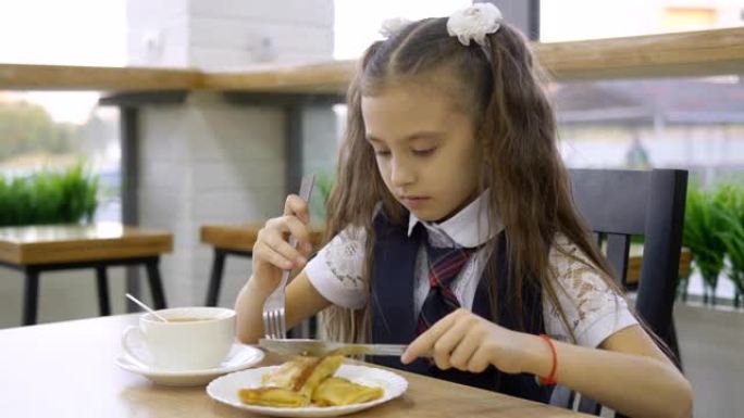 穿着校服的学生小学坐在学校食堂的桌子旁吃饭。