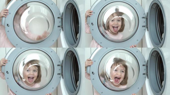 小滑稽女孩玩洗衣机舱口的特写。孩子透过舱口，周围的傻瓜，微笑和大笑