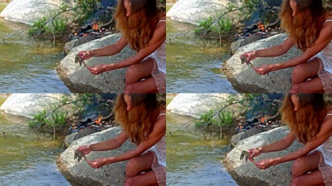 侧视图长发女孩在河岸上把虾放在棍子上