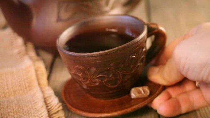 女人的手把一杯茶和糖果冰糖放在木桌上。背景上的茶壶