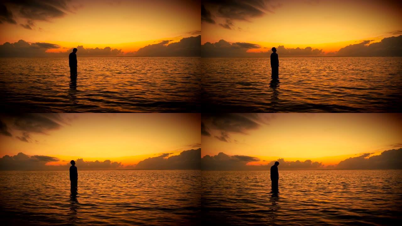 在五颜六色的日出或日落时，站在海洋中祈祷的人的剪影