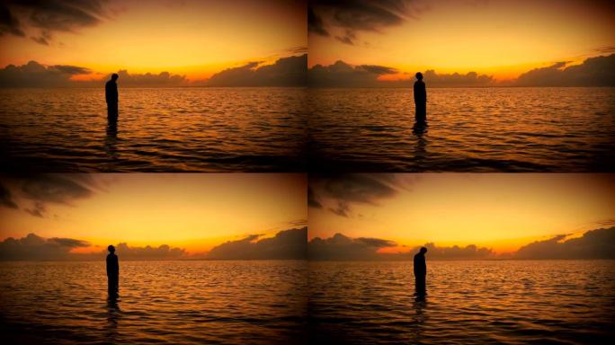 在五颜六色的日出或日落时，站在海洋中祈祷的人的剪影