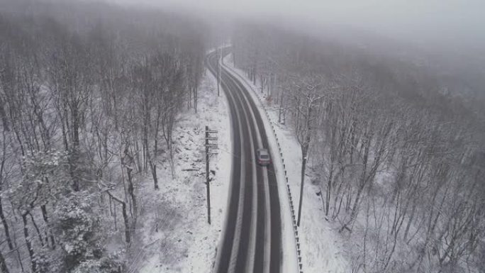 在降雪下驾驶高速公路穿过森林的汽车。无人机航拍视频与前摄像机朝着汽车接近，然后跟随另一辆车。