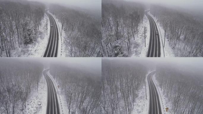 在降雪下驾驶高速公路穿过森林的汽车。无人机航拍视频与前摄像机朝着汽车接近，然后跟随另一辆车。