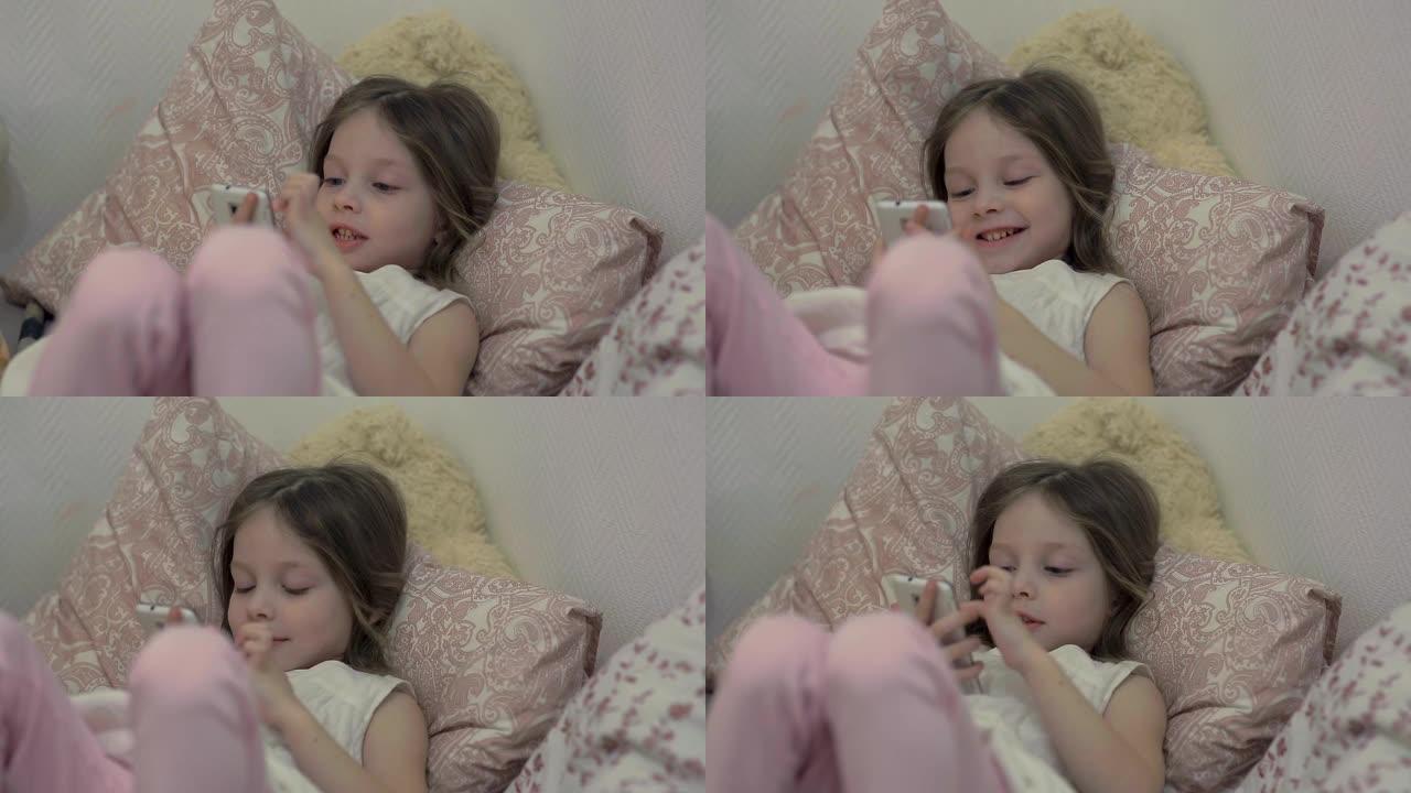 一个小女孩躺在床上，在智能手机屏幕上观看动画片，儿童和数字技术