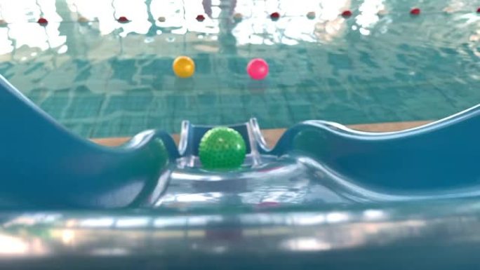 绿色球在水滑梯上滚落到游泳池