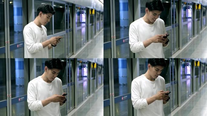 亚洲男子在地铁等车时用智能手机指着手机。亚洲男人和女人。