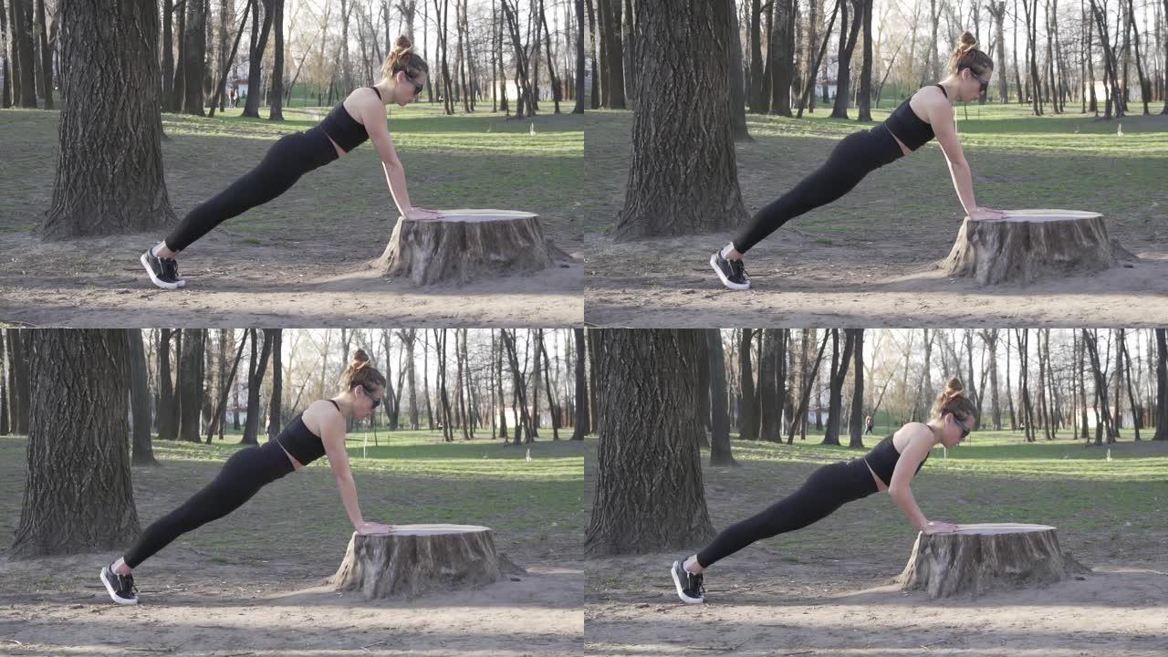 在公园的木头上做俯卧撑，适合在树林里锻炼的女人。在露天天然健身房锻炼。俯卧撑。有吸引力的女运动员锻炼
