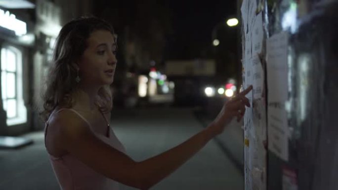 美丽的年轻女孩阅读贴在街上的广告