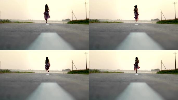 一个穿着长裙的美丽年轻女孩赤脚在路上奔跑，她快乐而无忧无虑。慢动作，焦点模糊