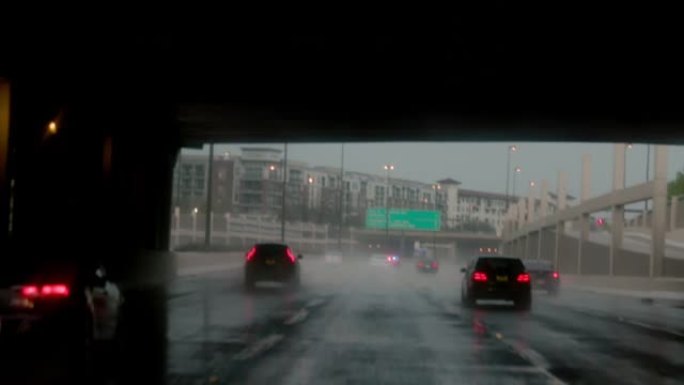 当车辆在高速公路上行驶时，雨刷行驶，远处的警笛声响起，挡风玻璃被雨滴覆盖。