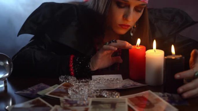年轻的神秘巫师坐在黑暗的房间里，主演三根蜡烛，普通女巫表演黑色仪式，照片和死亡拼写。吉普赛人用手做药
