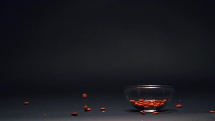 橙色糖果慢动作落在玻璃碗中，黑色黑板纹理背景上有复制空间