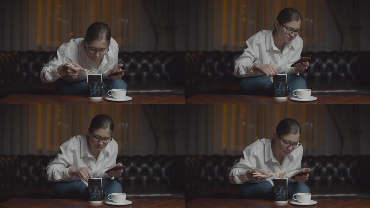 30多岁戴眼镜的女人用筷子吃亚洲盒饭看着笔记本电脑显示器。深夜孤独的家庭晚餐与小玩意。