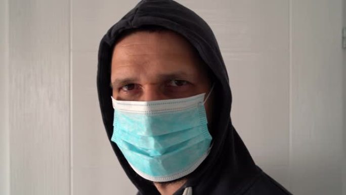 高加索成年男子的肖像，头上戴着防护医用口罩和兜帽，以防止病毒细菌大流行污染，对着镜头近距离走开