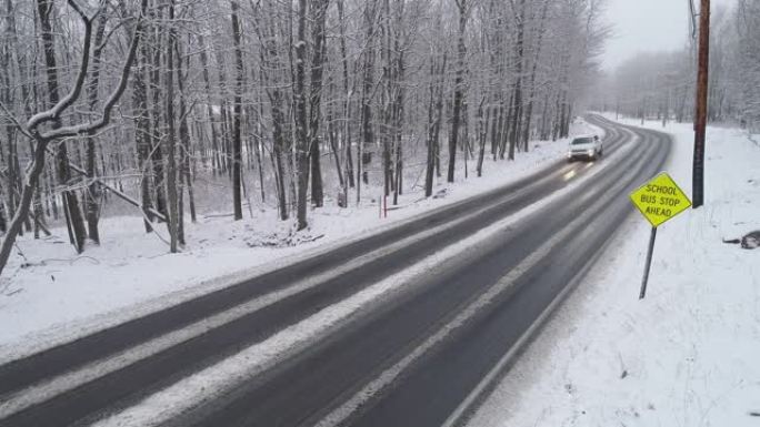 皮卡车和其他汽车在降雪下驾驶高速公路穿过森林。带有静态摄像机的无人机航拍视频。